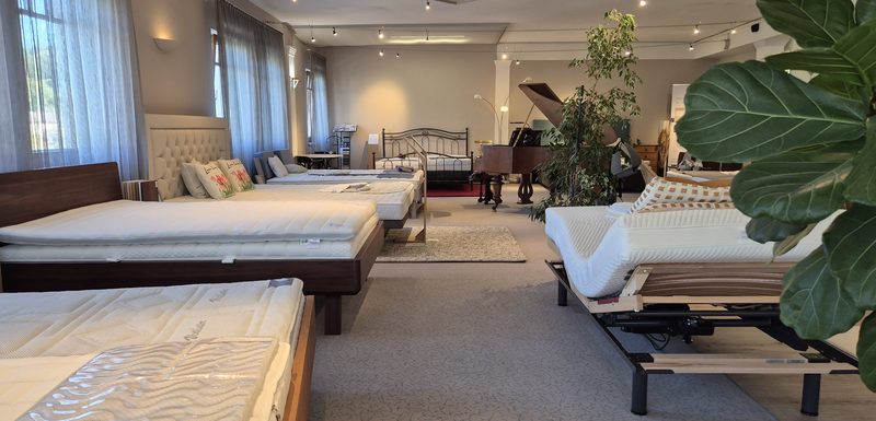 Blick durch den Showroom: Betten und Matratzen in einer Reihe, Tageslicht von den Fenstern
