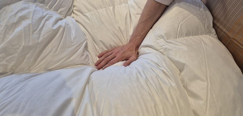 Eine Hand drückt in eine Daunendecke, der Stoff legt sich in weiche Falten