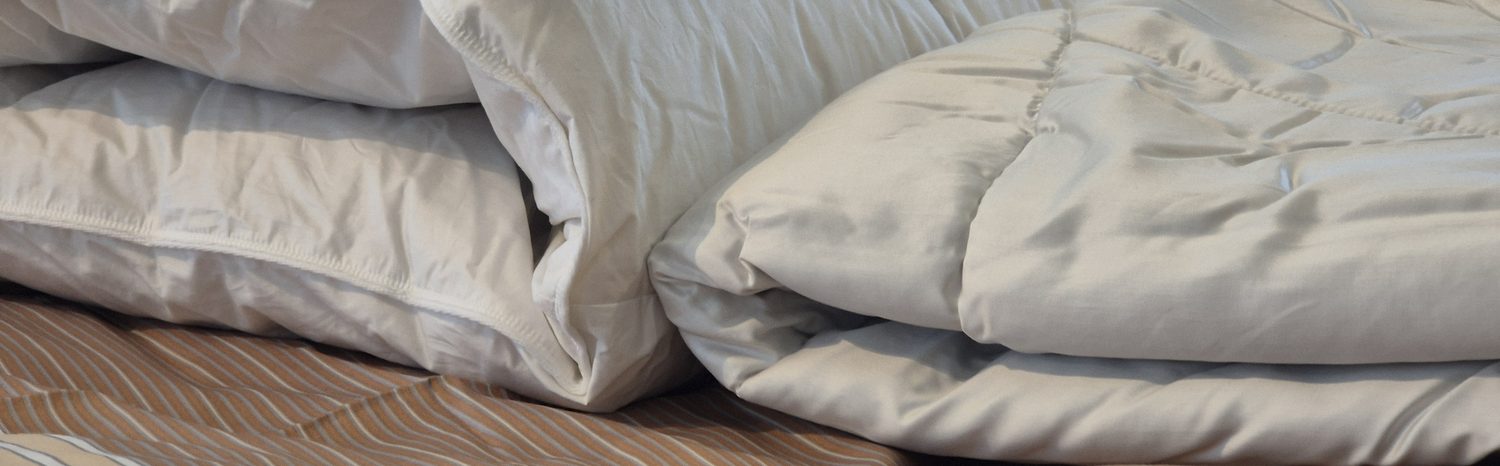 Zwei zusammengelegte Zudecken liegen nebeneinander auf einem Bett, von der Seite beleuchtet.